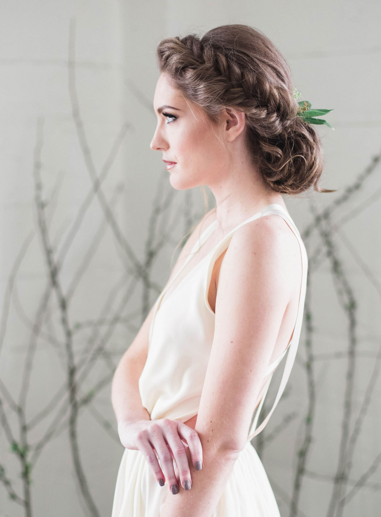 bride with braided hair that goes into a low bun and some greenery