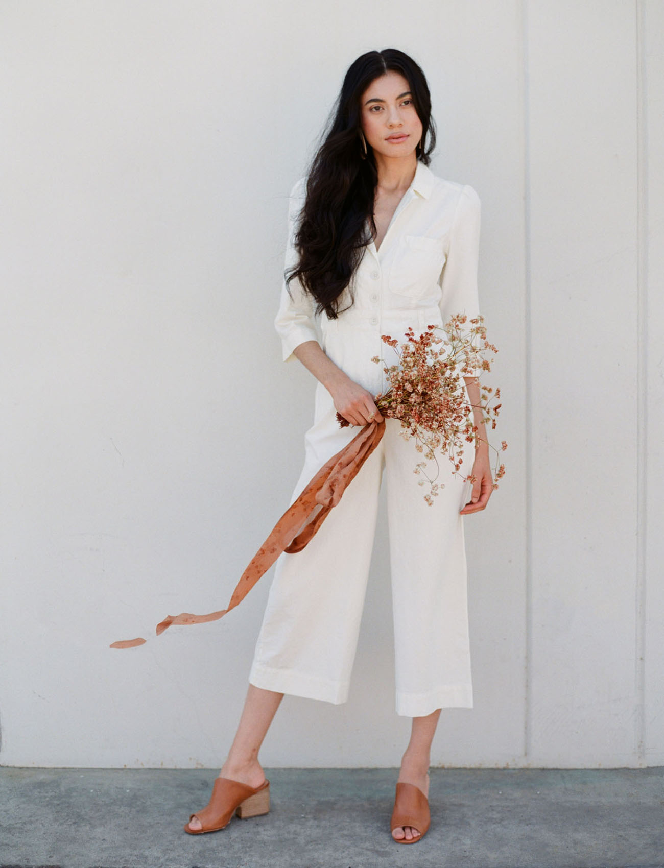 Bride in white pantsuit with rust colored single flower bouquet