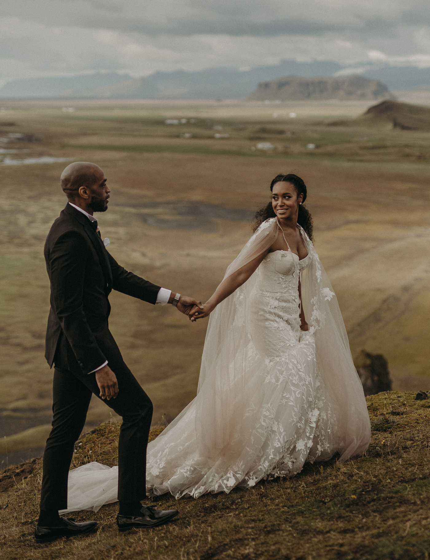 bride and groom walking up a mountain in a bridal cape