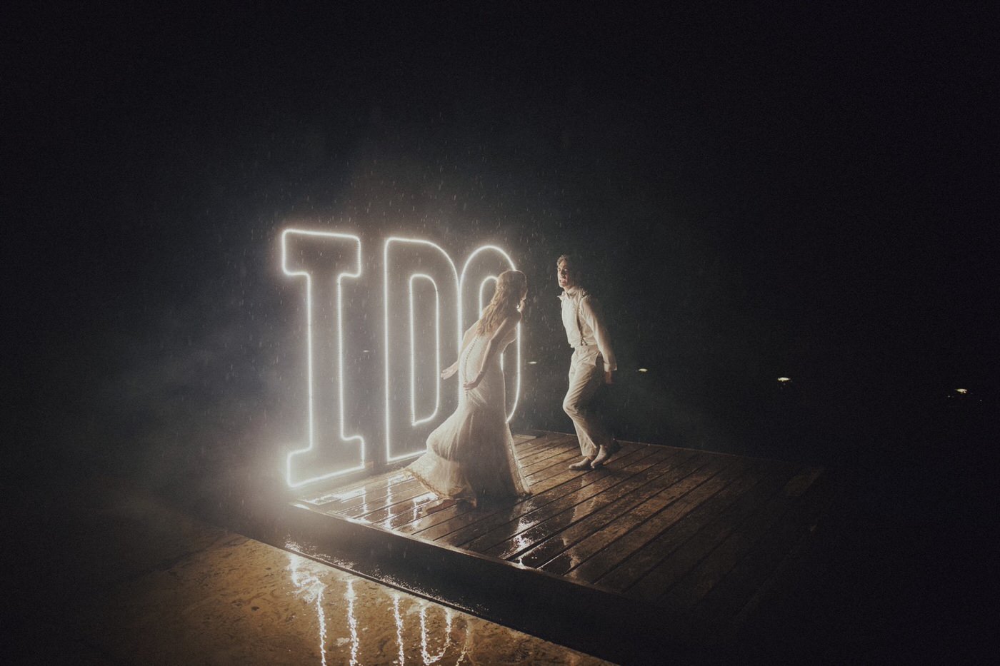couple dancing in the rain at their wedding reception with I Do letters