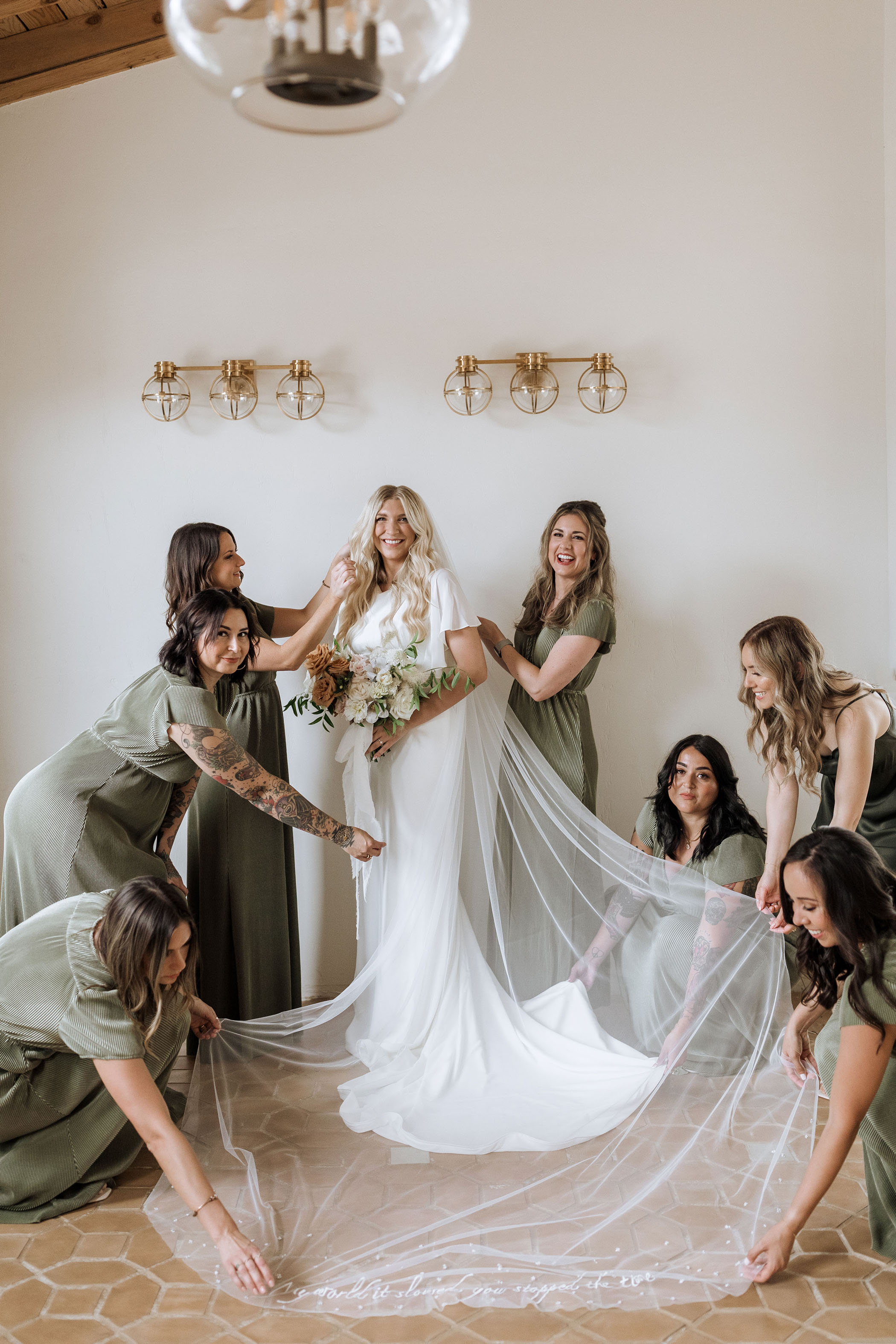 bridesmaids in olive green dresses helping a bride fix her veil