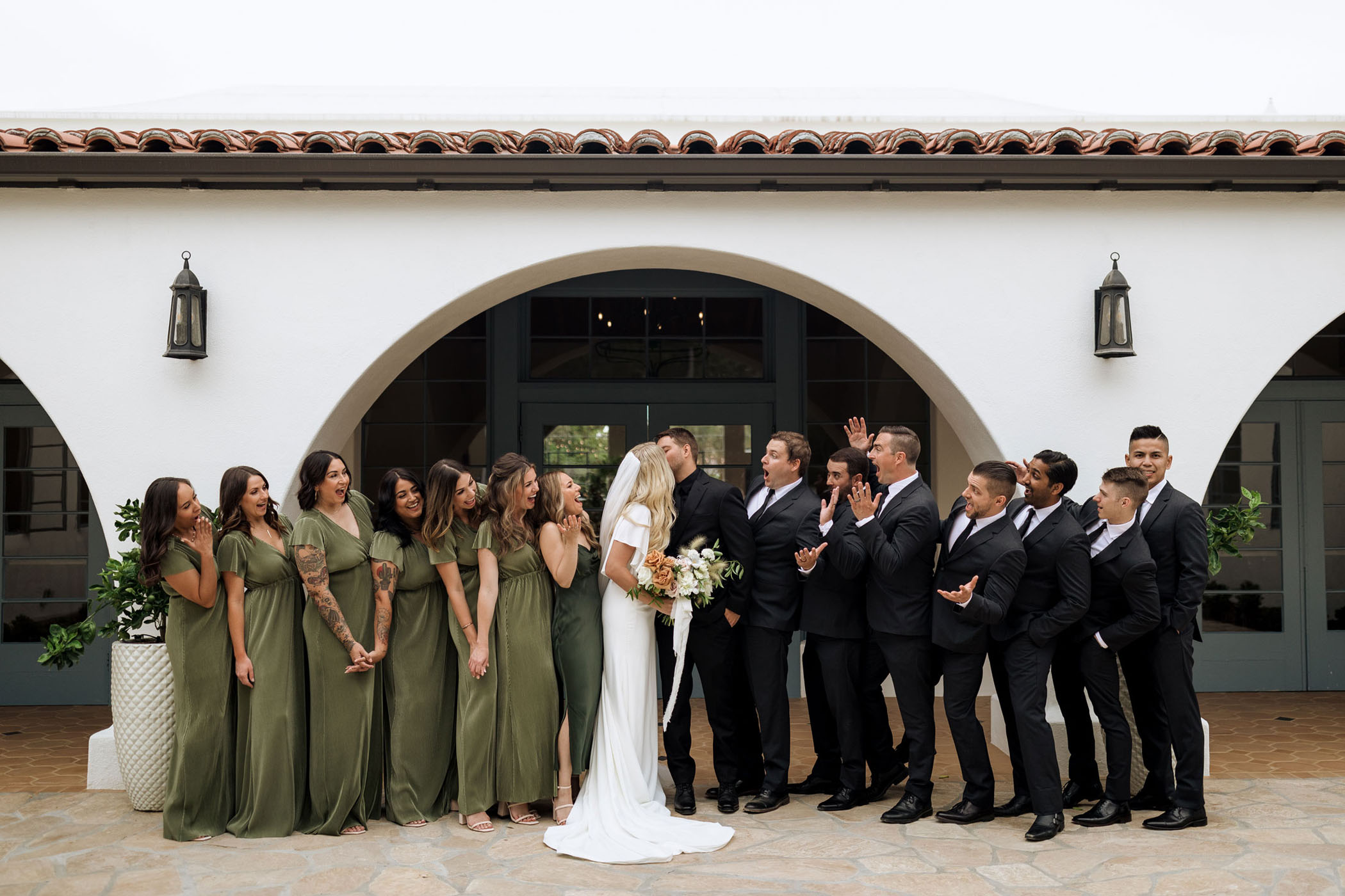 bridesmaids and groomsmen smile as bride and groom share a kiss on their wedding day