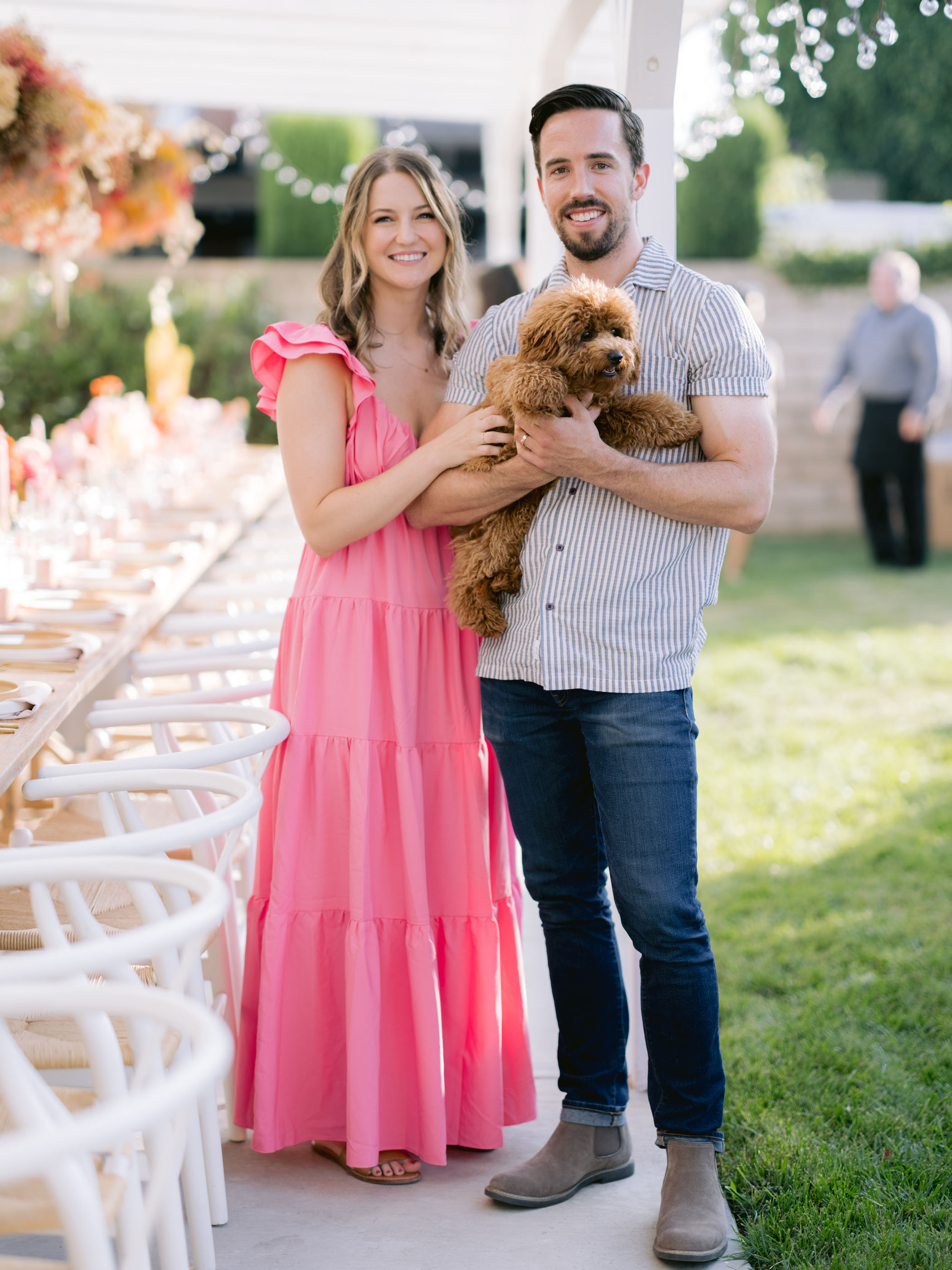 woman in pink tiered dress smiling with her husband and puppy