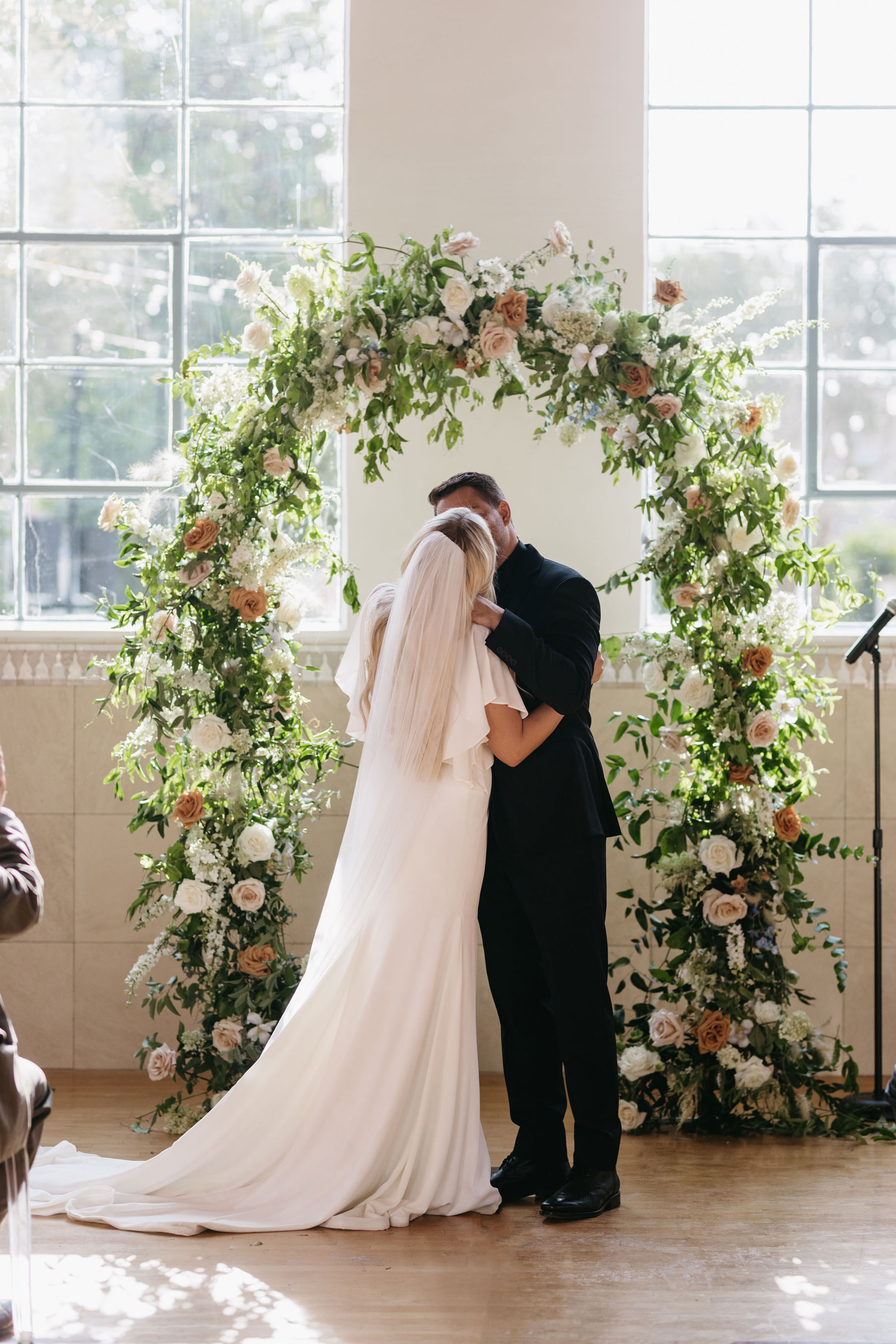 bride and groom sharing their first kiss in front of a greenery and floral ceremony arch