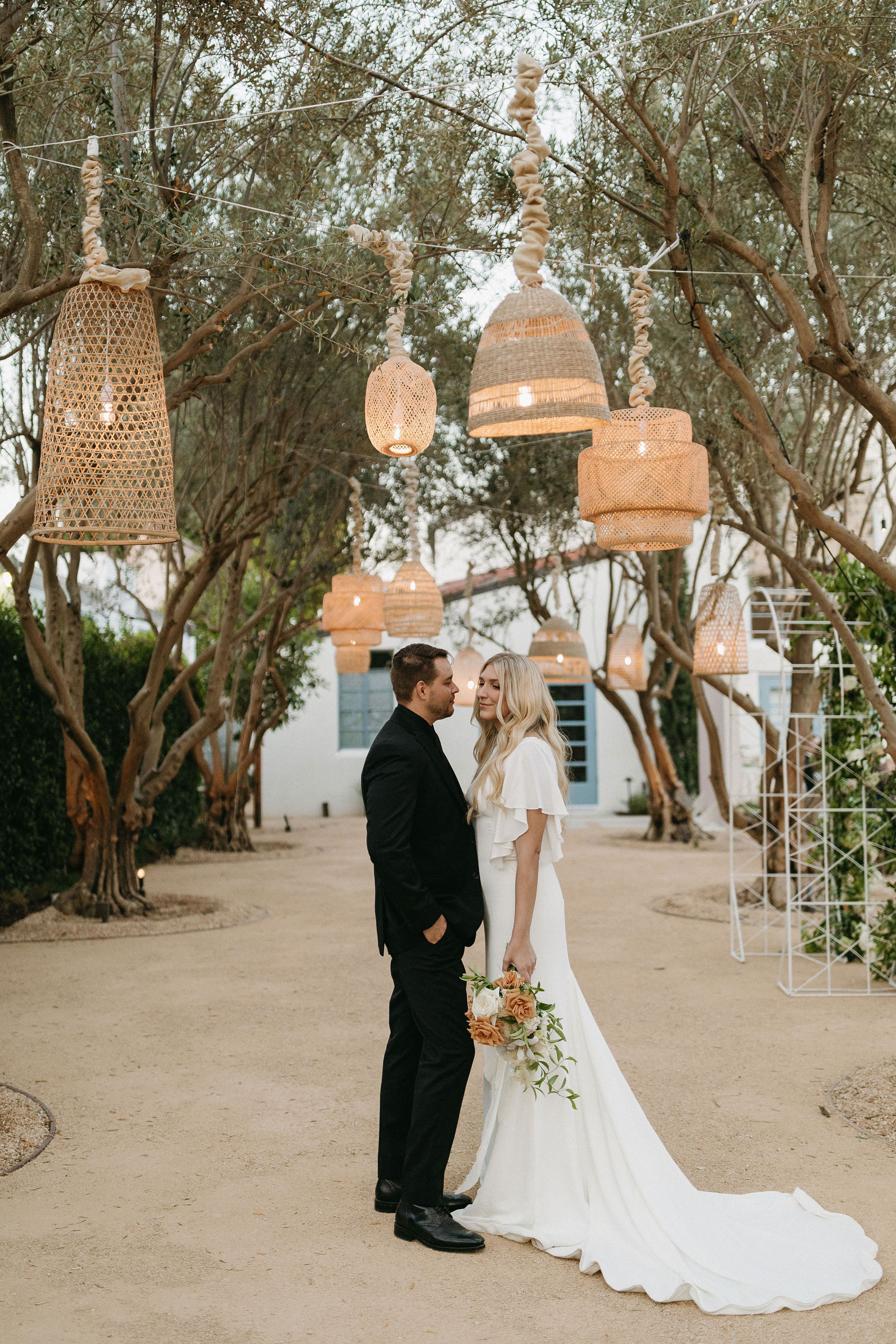 bride and groom standing under outdoor rattan lanterns