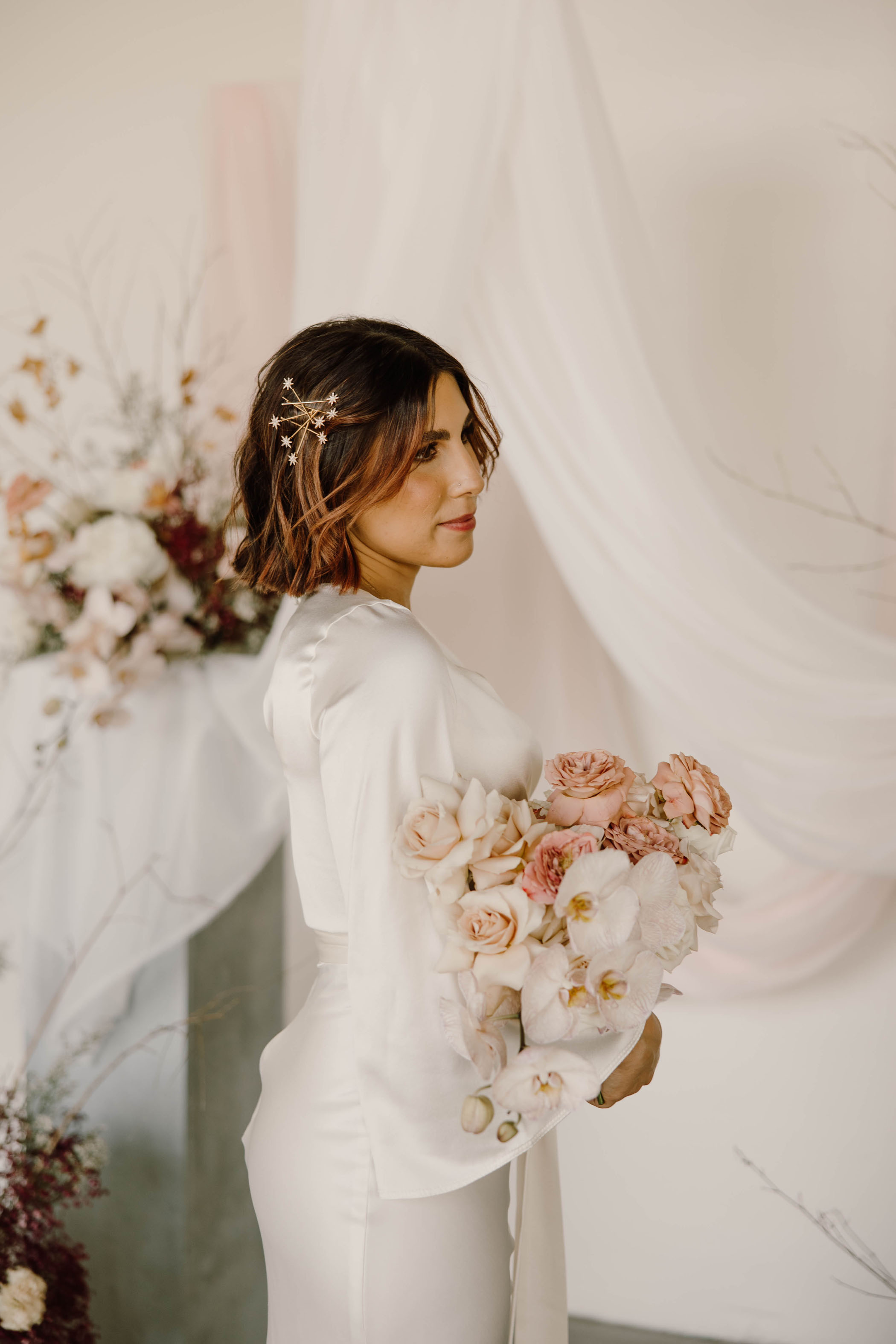 bride wearing long sleeved silk wedding dress holding a pink orchid bouquet