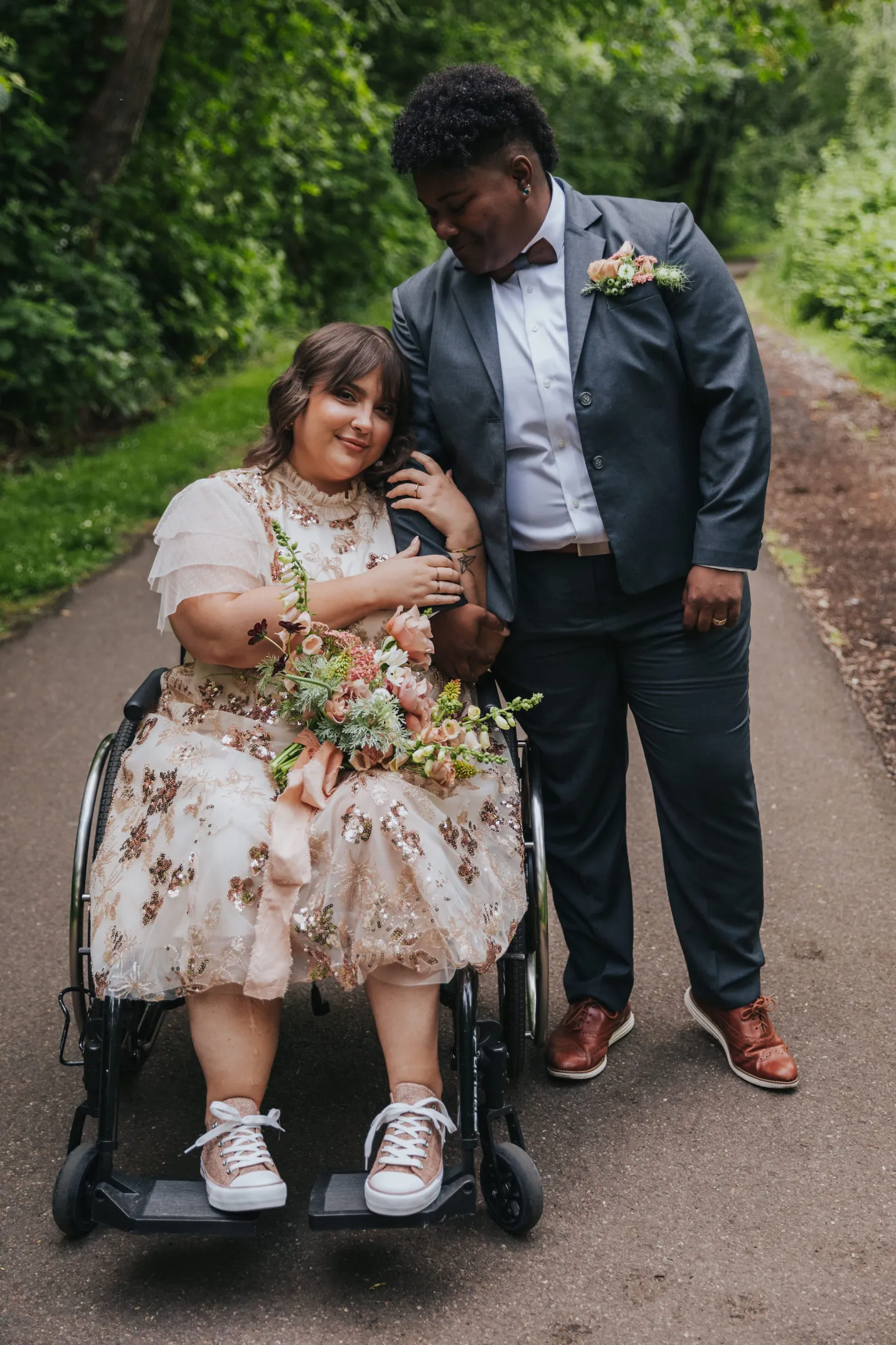 couple standing and sitting together for a planned photo at their wheelchair accessible wedding location on a greenery lined path